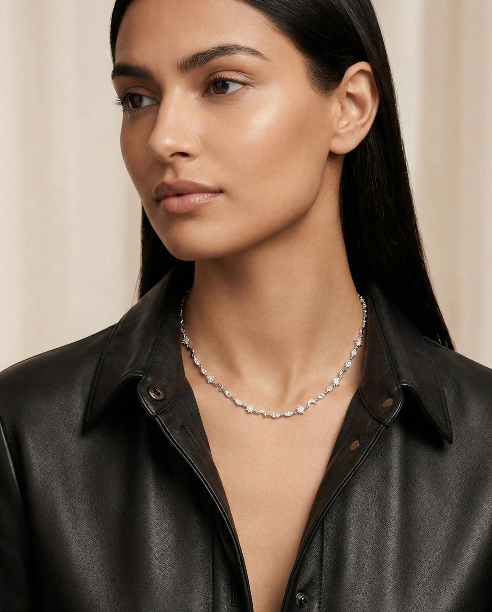 Woman wearing a black leather jacket and silver necklace with zircon stones against a beige backgrounds
